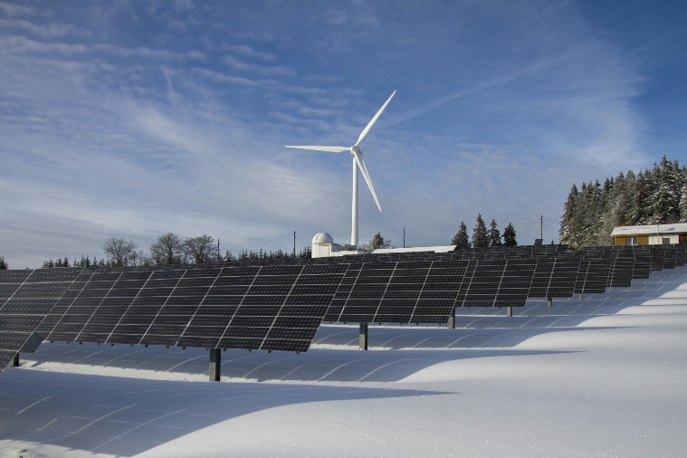 Solar panels in a snow-filled field and a windmill in the distance.